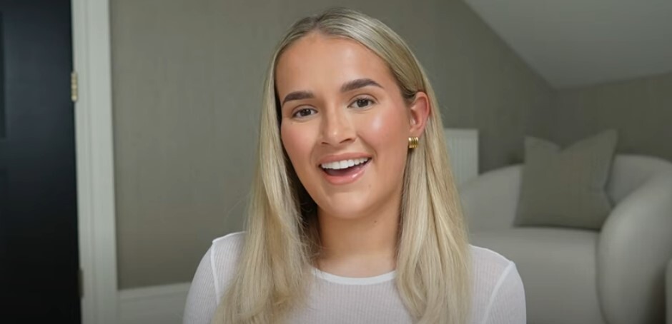 a blonde woman wearing a white shirt and gold earrings smiles