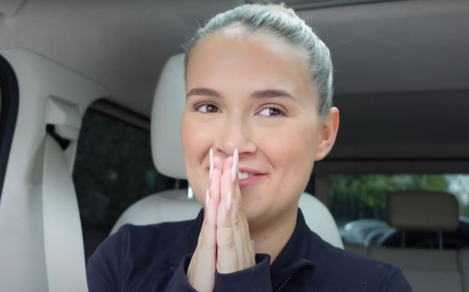 a woman sitting in a car with her hands folded in front of her face