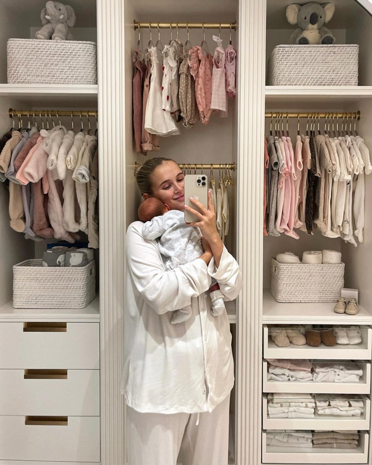 a woman holds a baby in front of a closet full of baby clothes