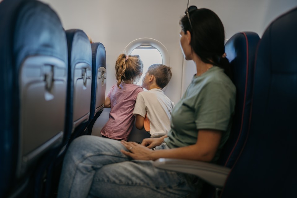 a woman and two children sit on an airplane looking out the window