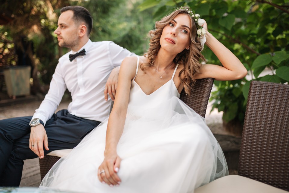 a bride and groom sit on a wicker chair with the bride wearing a flower crown