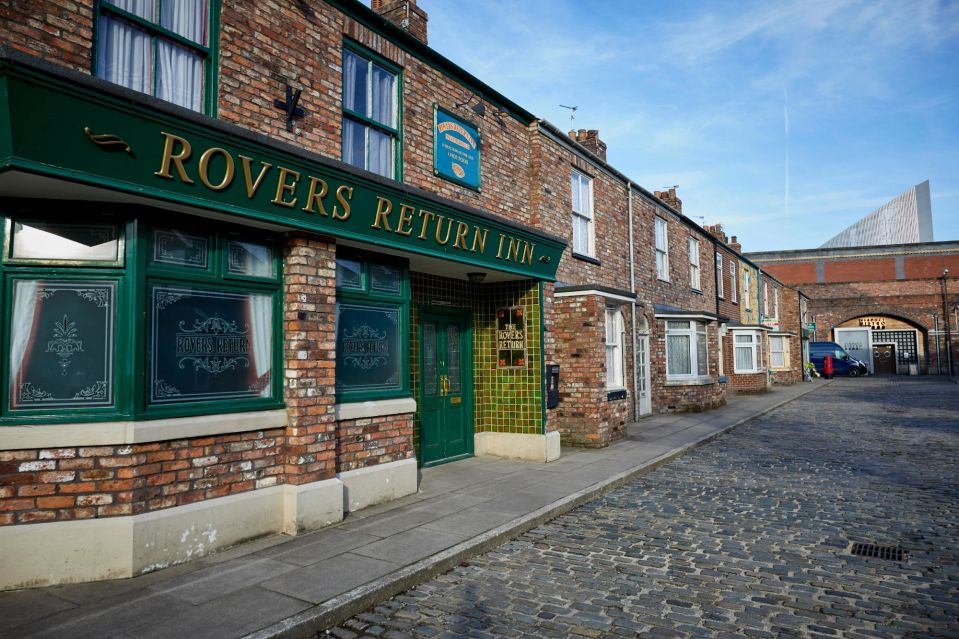 a row of brick buildings with a green sign that says rovers return inn