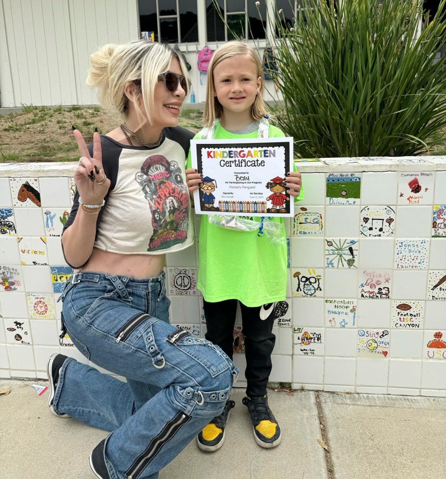 a woman kneeling next to a young girl holding a kindergarten certificate