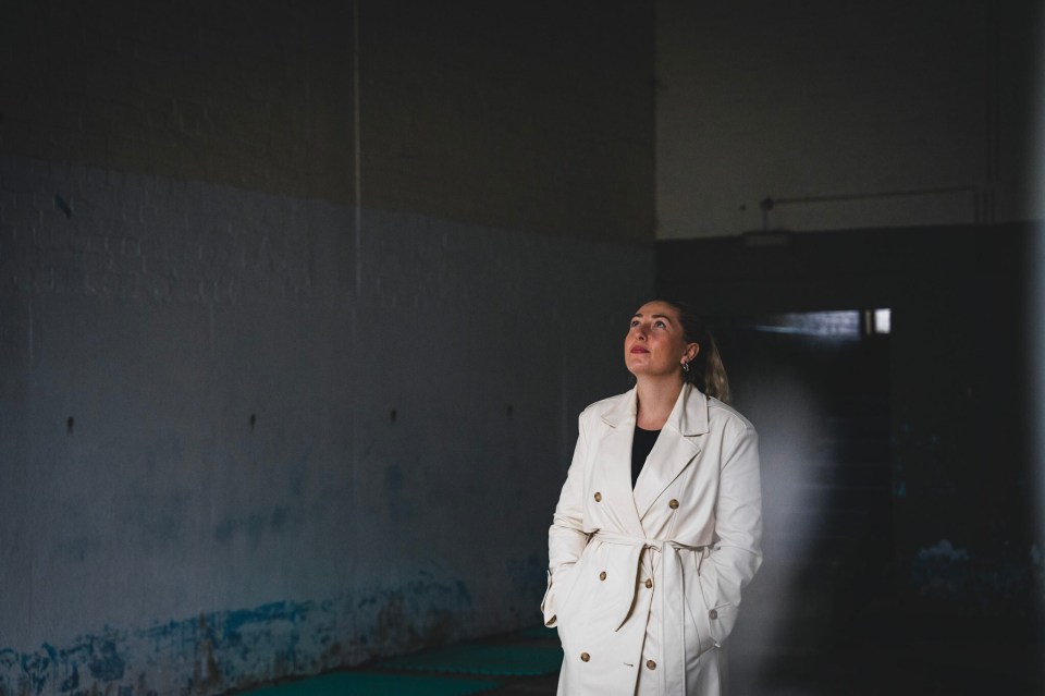 a woman in a white trench coat stands in a dark room