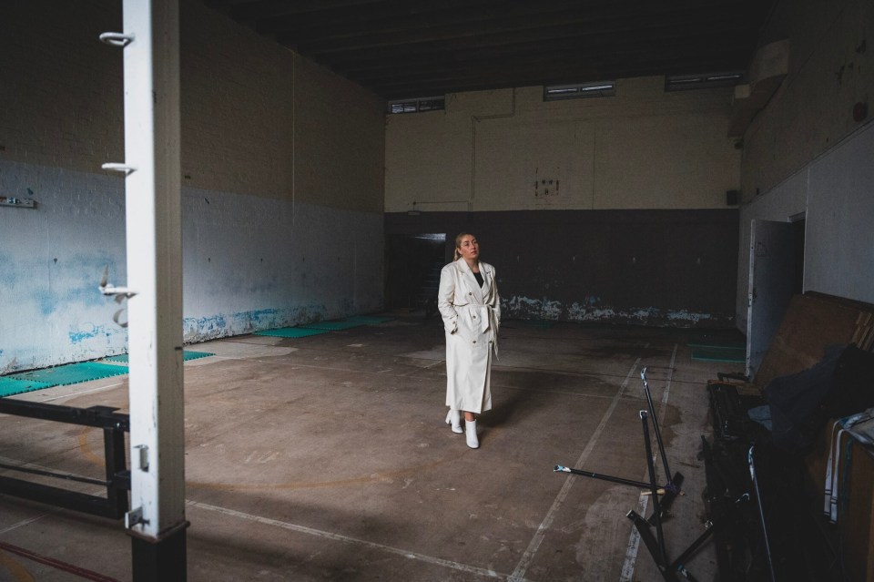 a woman in a white coat stands in an empty gym