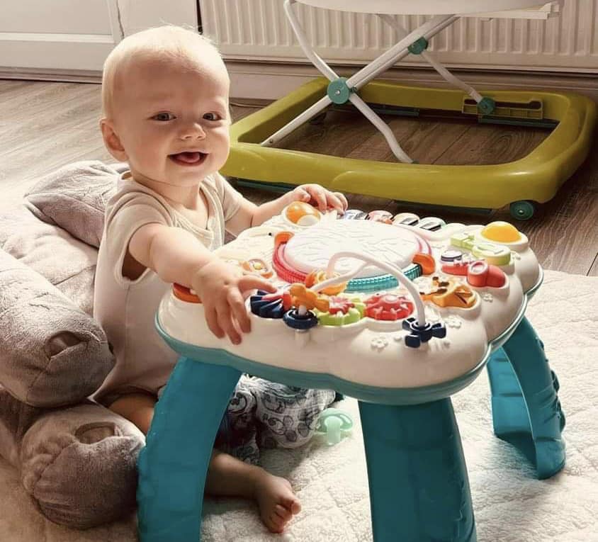 a baby is sitting at a table with a walker in the background