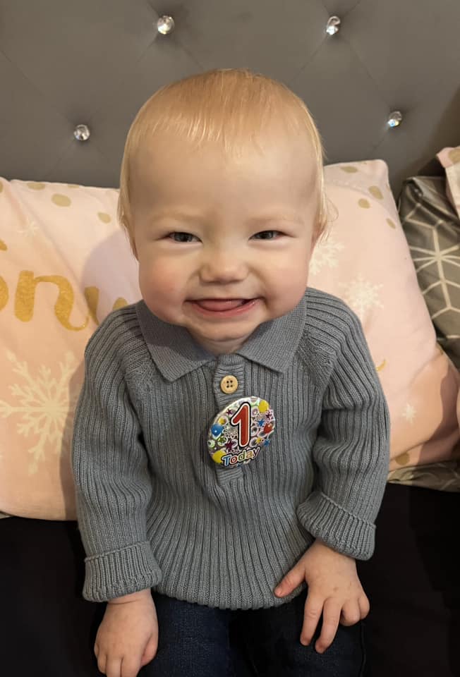 a baby wearing a sweater with a button that says 1 today