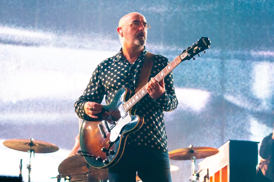 a bald man playing an epiphone guitar on stage