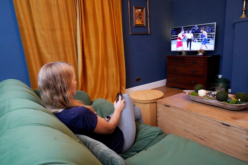 a woman sits on a couch watching a boxing match on a television