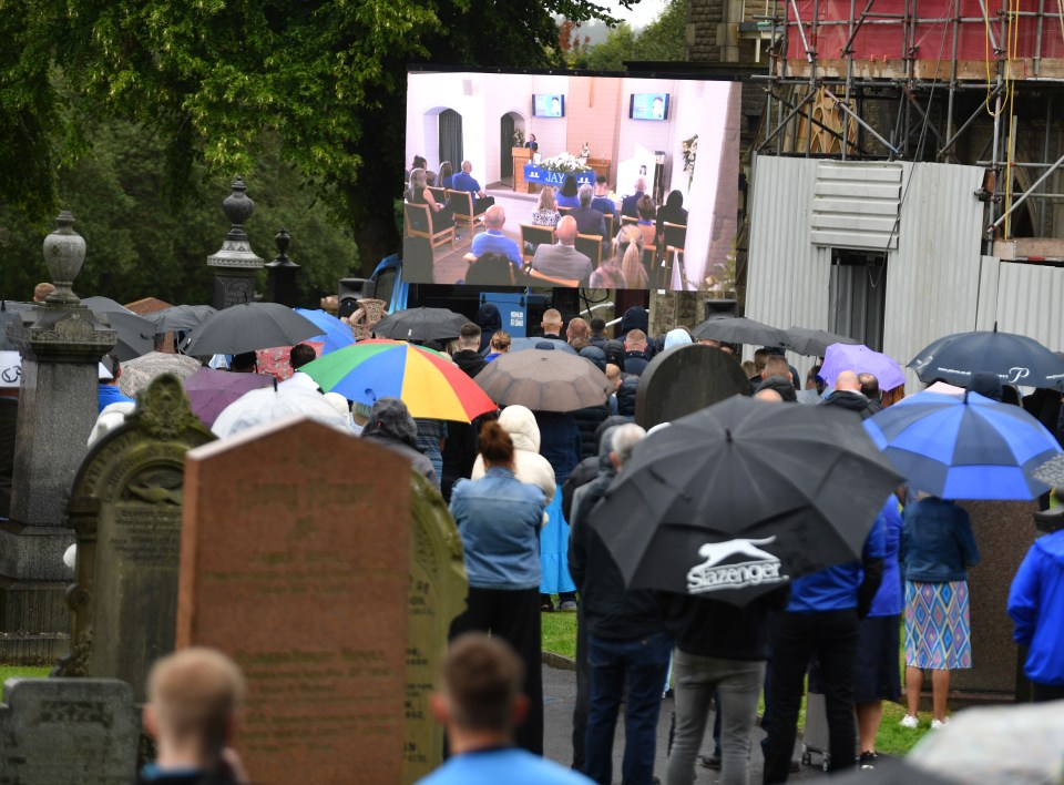 a crowd of people are watching a funeral on a large screen