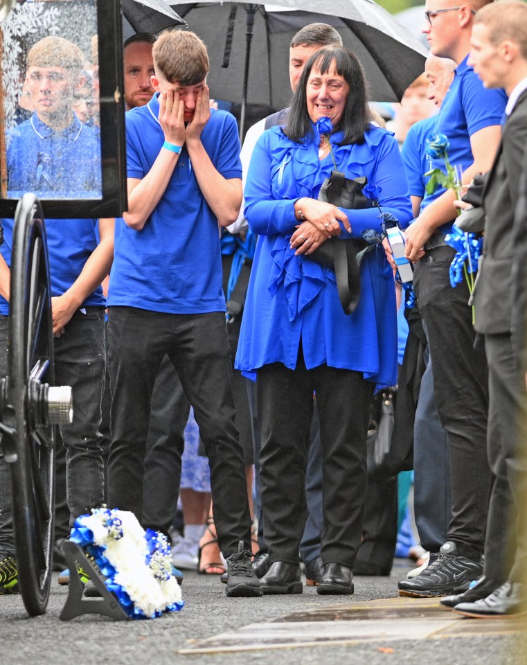 a group of people in blue shirts are standing in front of a coffin