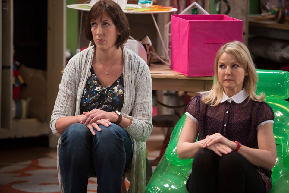 two women sit next to each other in a room with a pink box in the background