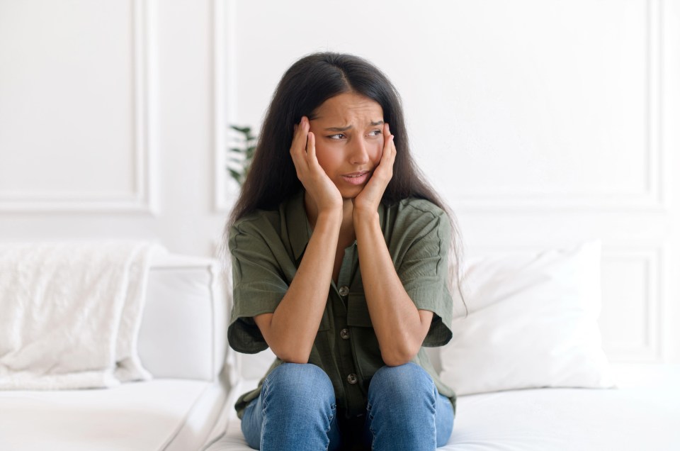 a woman sits on a couch with her hands on her face