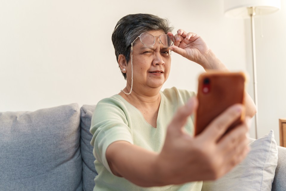 an older woman wearing glasses looks at her phone