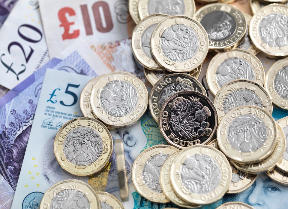 a pile of one pound coins sits on top of a pile of 20 and 5 pound notes