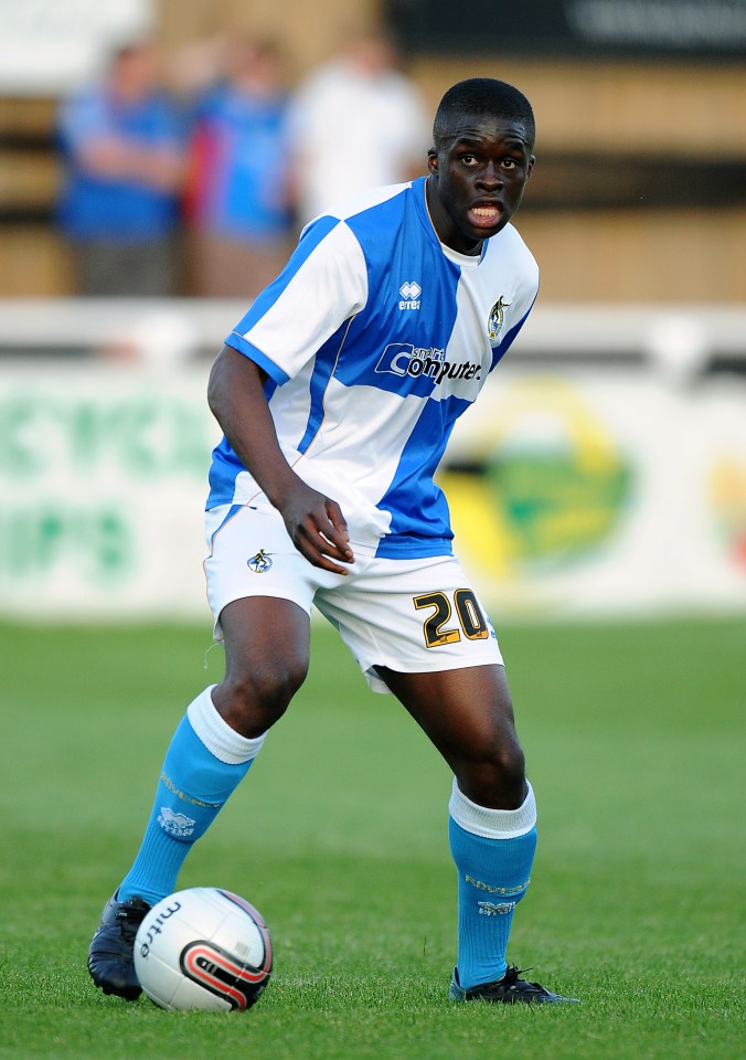 a man wearing a blue and yellow errea shirt smiles for the camera