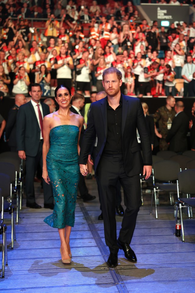 a man in a suit and a woman in a blue dress walk down a stage holding hands