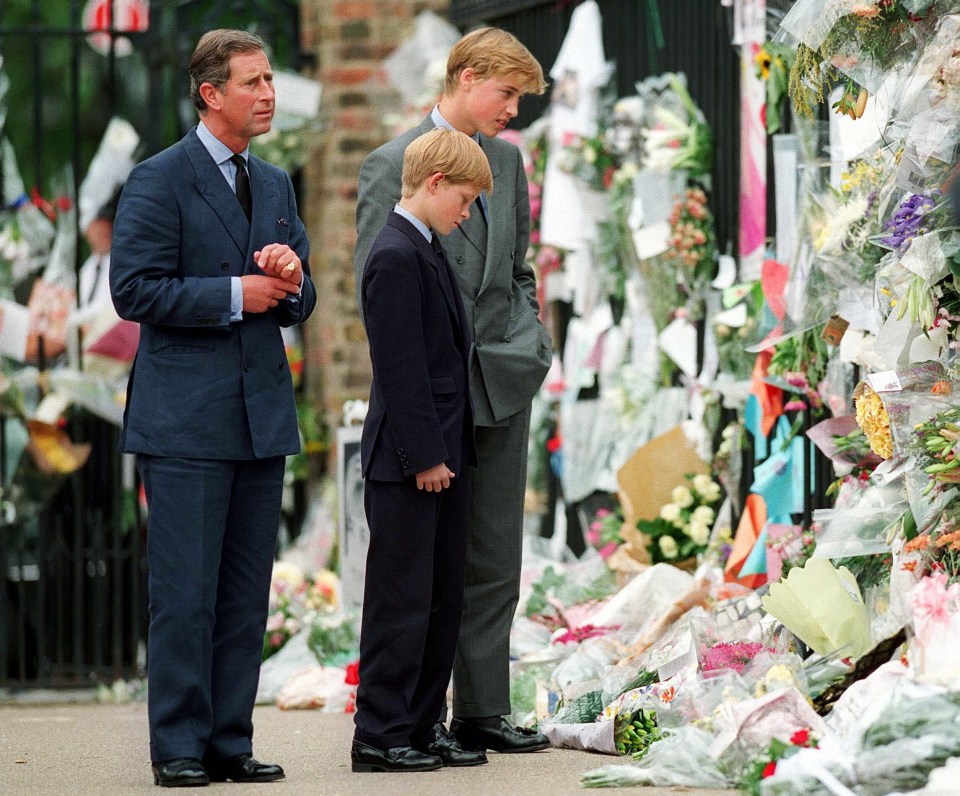 three men in suits stand in front of a wall of flowers