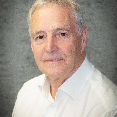 a man with gray hair is wearing a white shirt and looking at the camera .