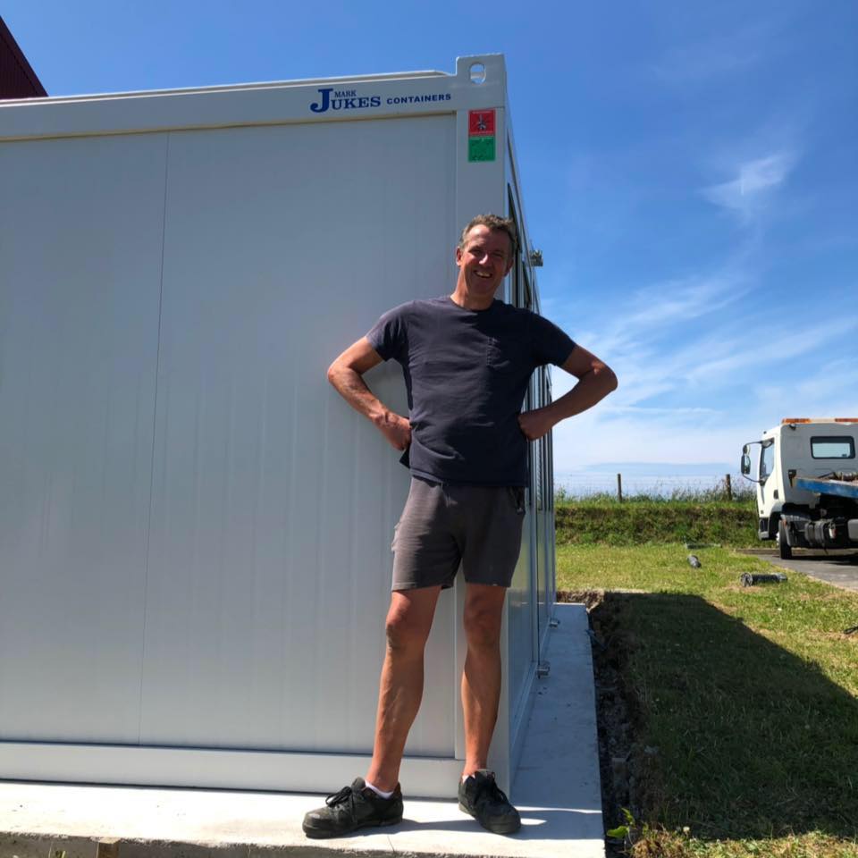 a man stands in front of a white jukes container