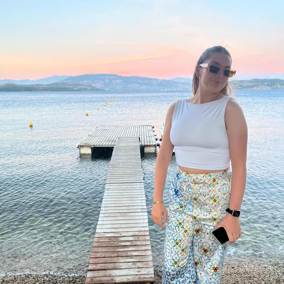 a woman wearing sunglasses stands on a dock overlooking a body of water