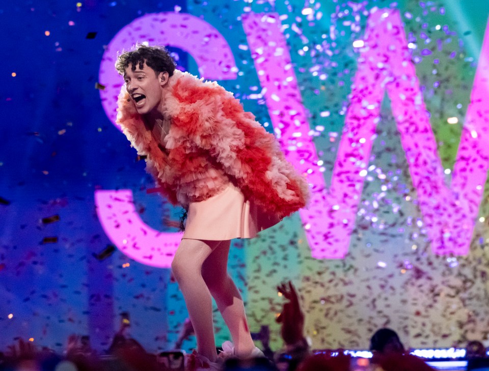 a man in a pink fur coat stands in front of a sign that says sw