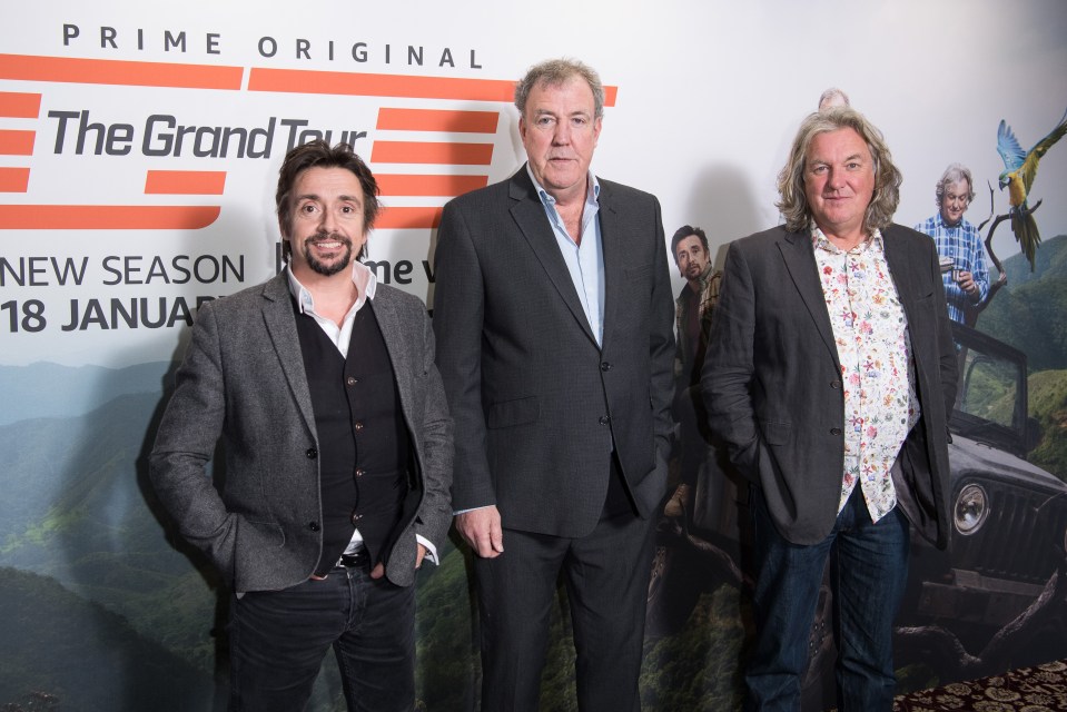 three men stand in front of a poster for the grand tour