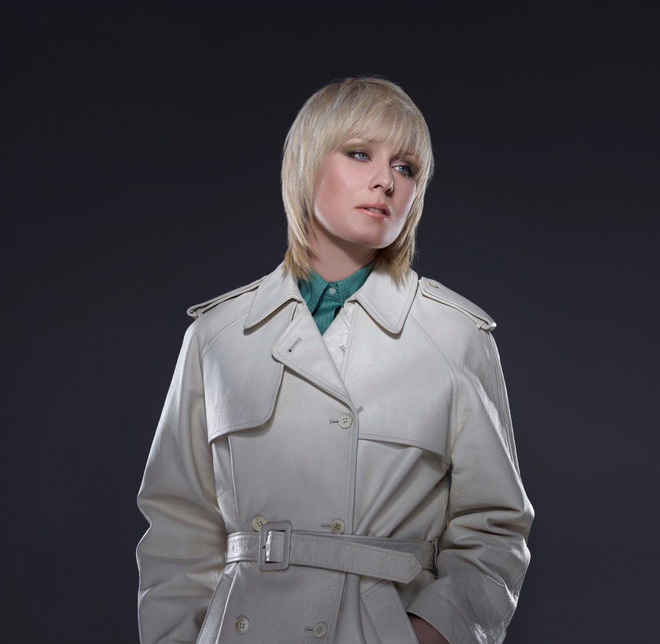 a woman wearing a white trench coat and a green shirt