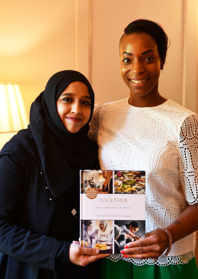 two women standing next to each other holding a book together