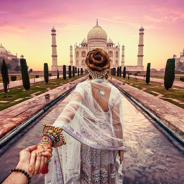 a woman in a white dress holds a man 's hand in front of the taj mahal