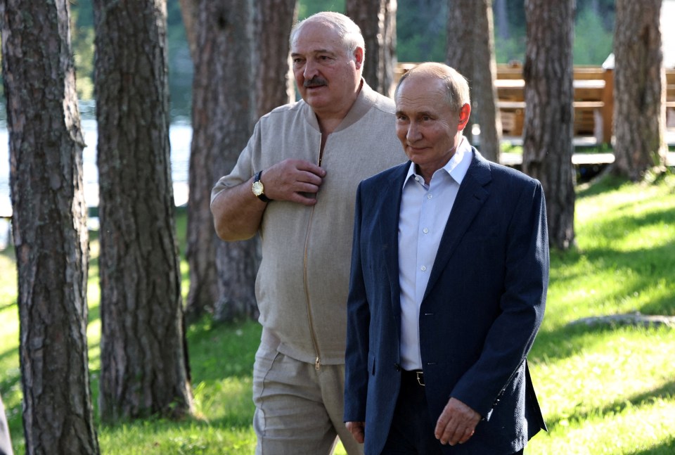 a man in a suit stands next to another man in a tan jacket