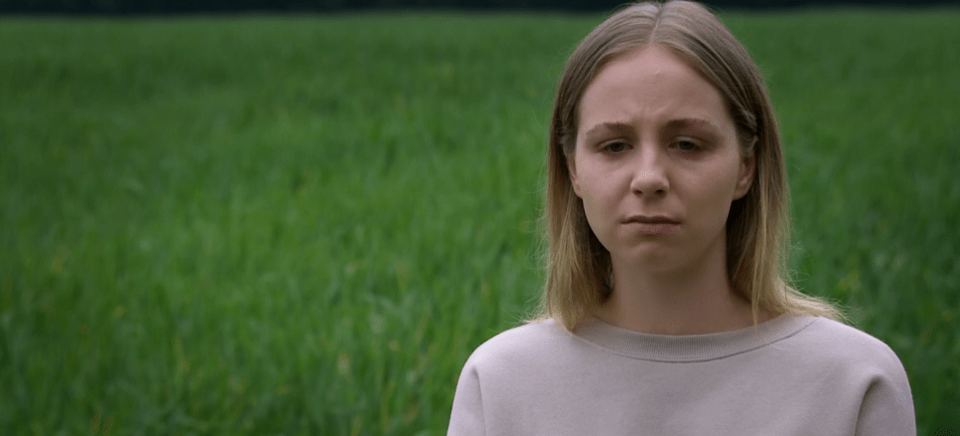 a woman in a white shirt stands in front of a green field