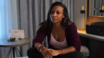 a woman in a purple sweater sits on a bed