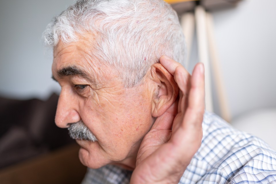 a man with gray hair and a mustache holds his hand to his ear