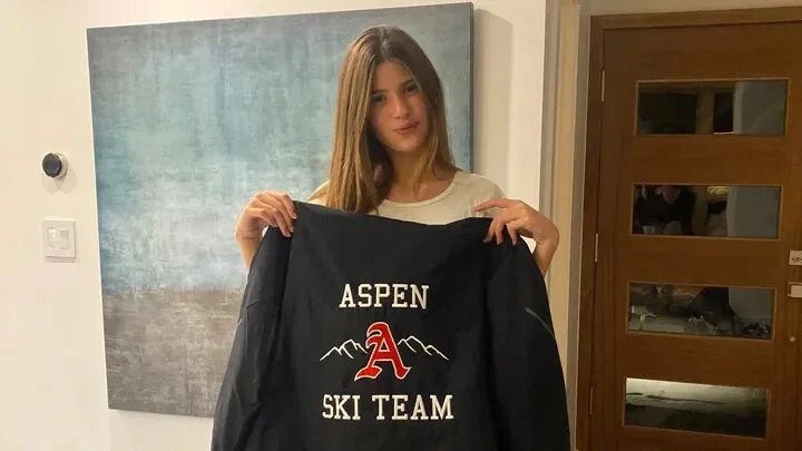 a young woman is holding a black jacket that says aspen ski team .