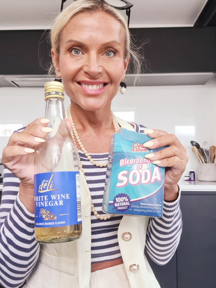 a woman holding a bottle of white wine vinegar and a bag of bicarbonate of soda