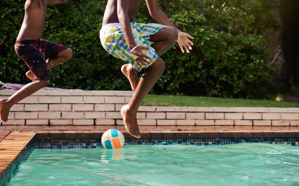 two boys are jumping into a swimming pool with a ball