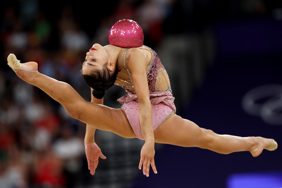 a female gymnast performs a split with a pink ball on her head