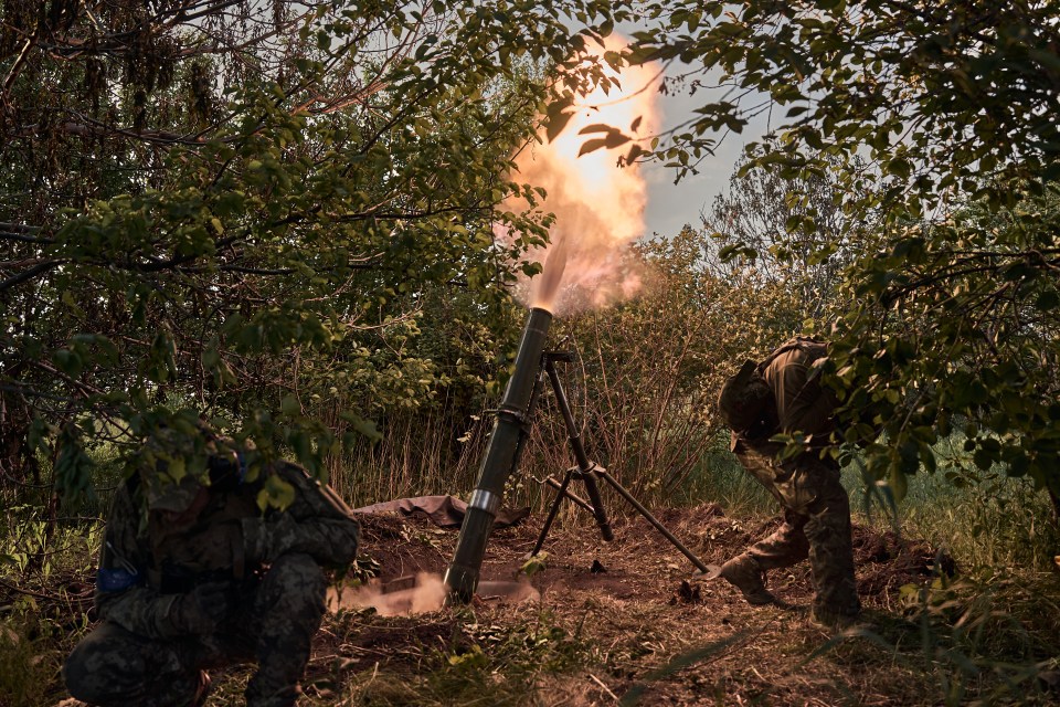 two soldiers are looking at a flame coming out of a mortar