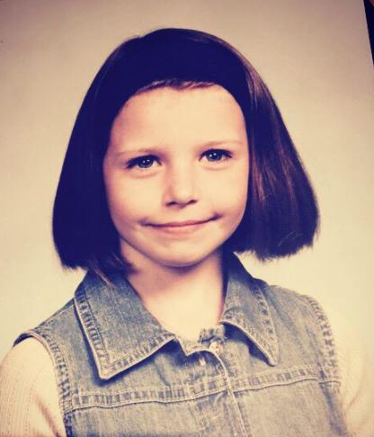 a young girl with short hair is wearing a denim shirt and smiling for the camera .