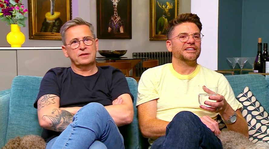 two men are sitting on a blue couch with their arms crossed