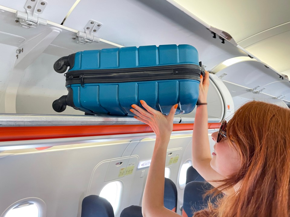 a woman is putting a blue suitcase in the overhead luggage compartment of an airplane