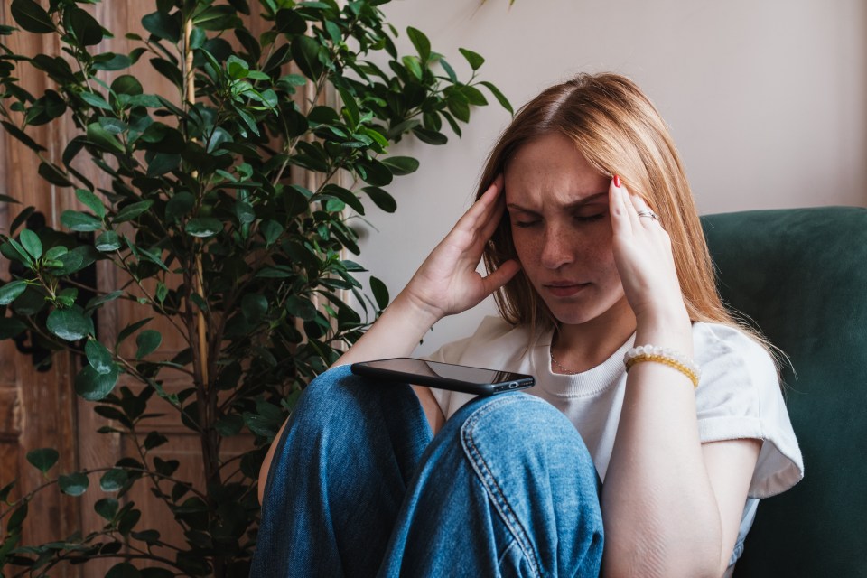 a woman sitting in a chair holding her head while looking at her phone