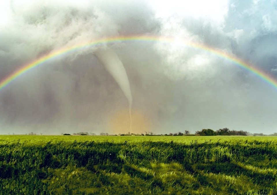 a tornado in a field with a rainbow in the background