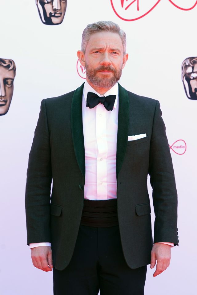 a man in a tuxedo stands on a red carpet