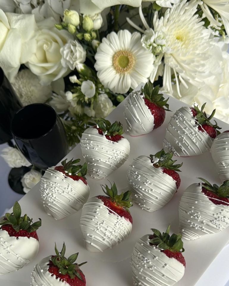 white chocolate covered strawberries on a white plate with flowers in the background