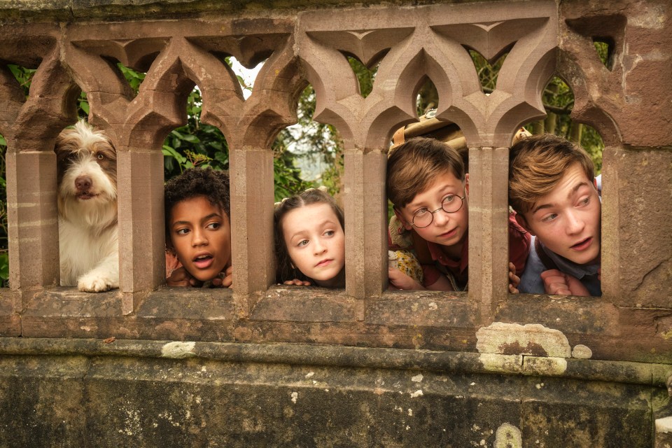 a group of children and a dog peeking over a stone fence