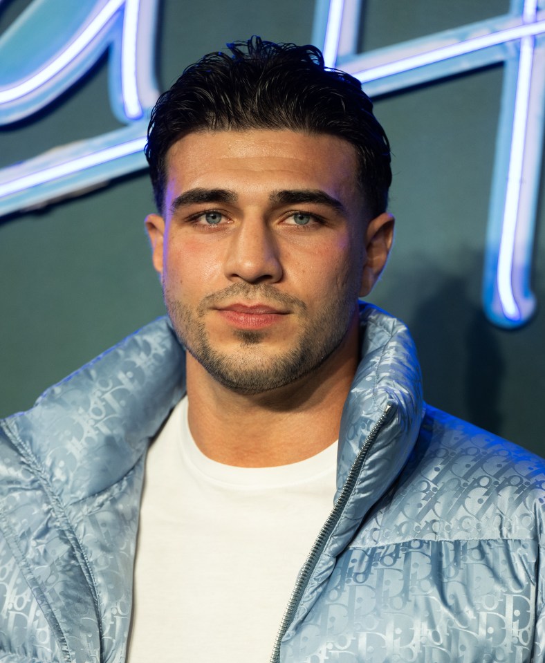 a man wearing a blue dior jacket stands in front of a neon sign