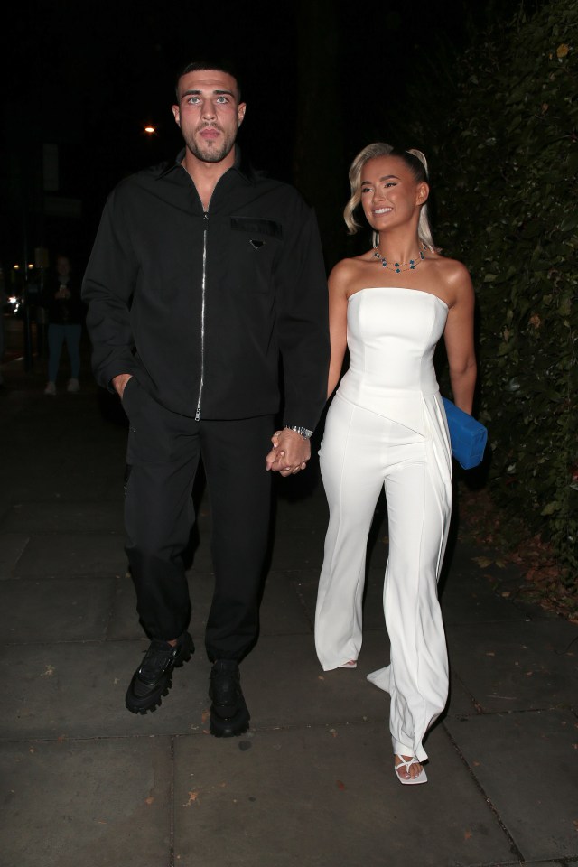 a man in a black jacket is holding hands with a woman in a white jumpsuit