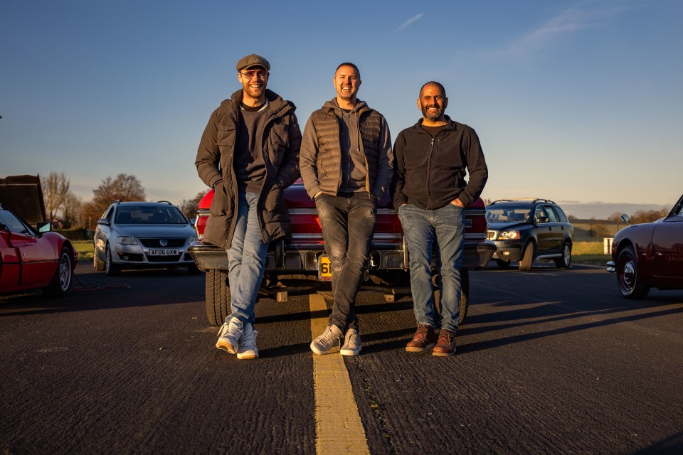 Three men sitting on the back of a red car.